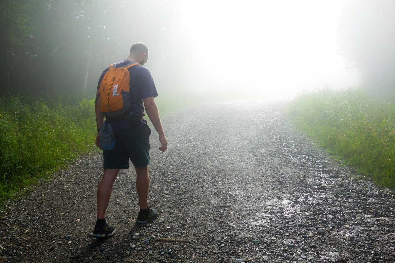 a man with a backpack walking down a foggy road